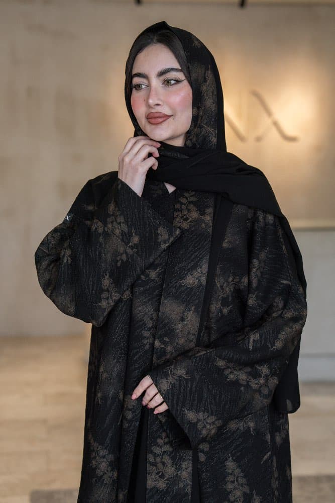 تصميم جاكار فاخر باللون الأسود والذهبي عباية باللون الأسود من قماش جاكار فاخر تحمل نقشات زهرية ذهبية منسجمة تمنحها حضوراً راقياً في كل مناسبة، قطعة تجمع بين الفخامة الهادئة والأناقة التي تلفت الأنظار قماش جاكار بنقشات ذهبية مميزة قماش جاكار ذو ملمس مميز يحمل نقشات زهرية ذهبية ضخمة منتشرة على خلفية سوداء غامقة، اللمعة الخفيفة في الخيوط الذهبية تضيف بريقاً دافئاً وراقياً يظهر في كل إضاءة، حافات أمامية بخط أسود أنيق يكمل شكل العباية بدقة الطرحه المتناسقة لإكمال إطلالتك تأتي العباية مع طرحة مصنوعة من نفس قماش الجاكار بنقشاته الذهبية مع بطانة من الشيفون الأسود الخفيف، تناسق تام يجعل إطلالتك متكاملة من الرأس حتى القدم