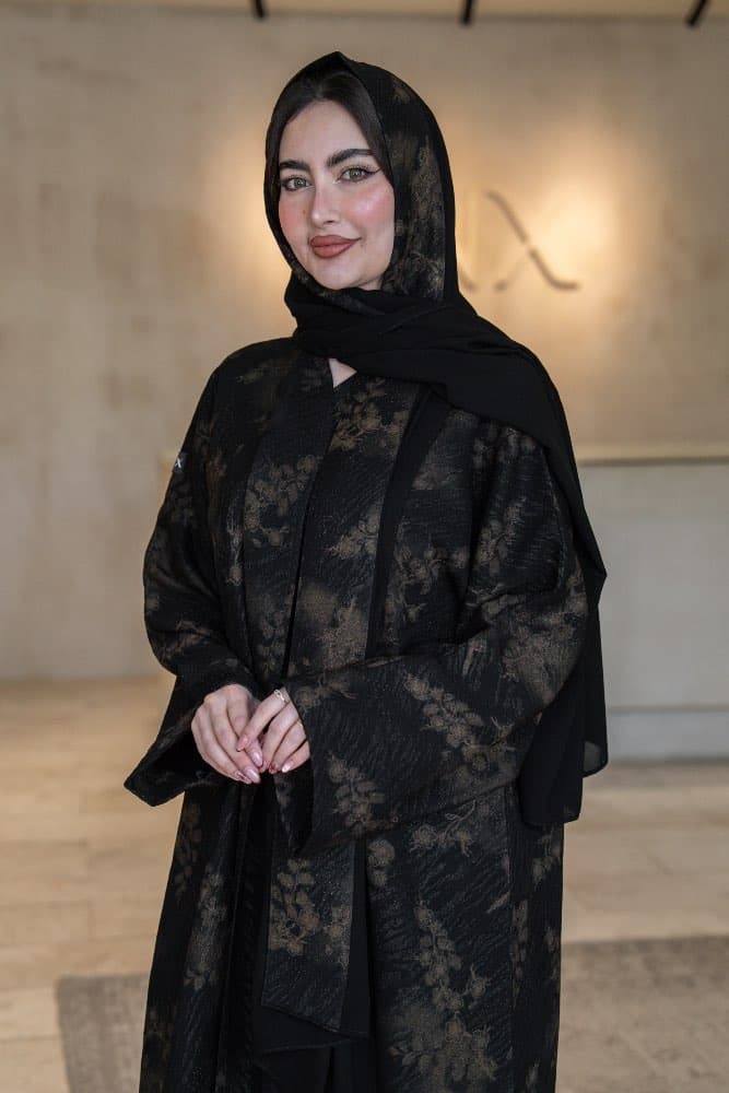 تصميم جاكار فاخر باللون الأسود والذهبي عباية باللون الأسود من قماش جاكار فاخر تحمل نقشات زهرية ذهبية منسجمة تمنحها حضوراً راقياً في كل مناسبة، قطعة تجمع بين الفخامة الهادئة والأناقة التي تلفت الأنظار قماش جاكار بنقشات ذهبية مميزة قماش جاكار ذو ملمس مميز يحمل نقشات زهرية ذهبية ضخمة منتشرة على خلفية سوداء غامقة، اللمعة الخفيفة في الخيوط الذهبية تضيف بريقاً دافئاً وراقياً يظهر في كل إضاءة، حافات أمامية بخط أسود أنيق يكمل شكل العباية بدقة الطرحه المتناسقة لإكمال إطلالتك تأتي العباية مع طرحة مصنوعة من نفس قماش الجاكار بنقشاته الذهبية مع بطانة من الشيفون الأسود الخفيف، تناسق تام يجعل إطلالتك متكاملة من الرأس حتى القدم